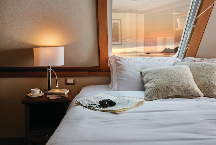 Binoculars and a newspaper on the bed in a Grand Suite on-board Silver Explorer