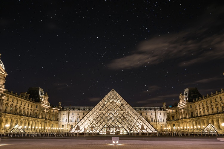 The pyramid of the Louvre illuminated at night under hundreds of stars