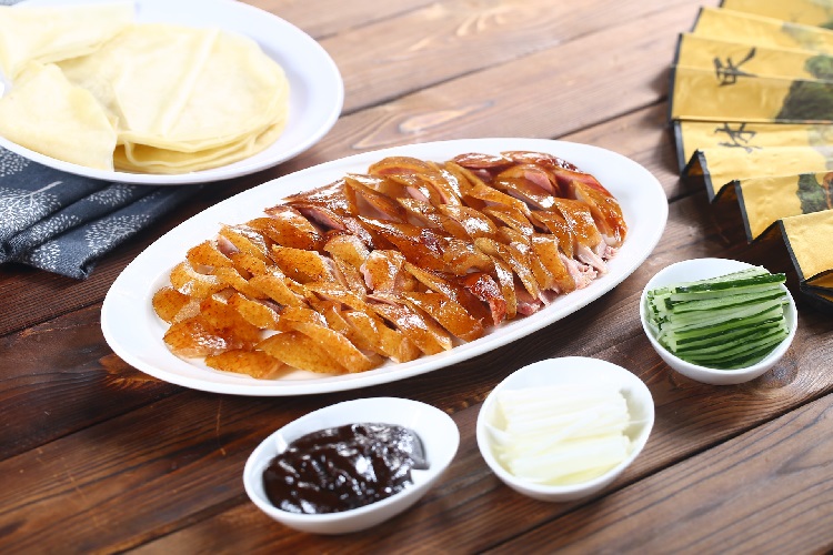 A plate of Peking duck surrounded by toppings and pancakes