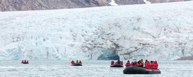 Expedition cruise guests driving away from a glacier in Zodiacs
